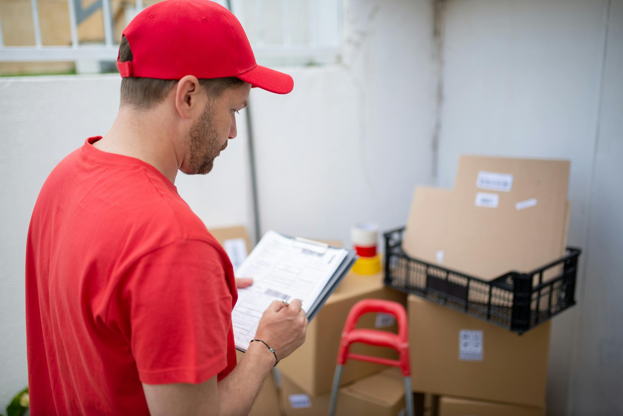Delivery person in red uniform checks packages. Outdoor location, Portugal.