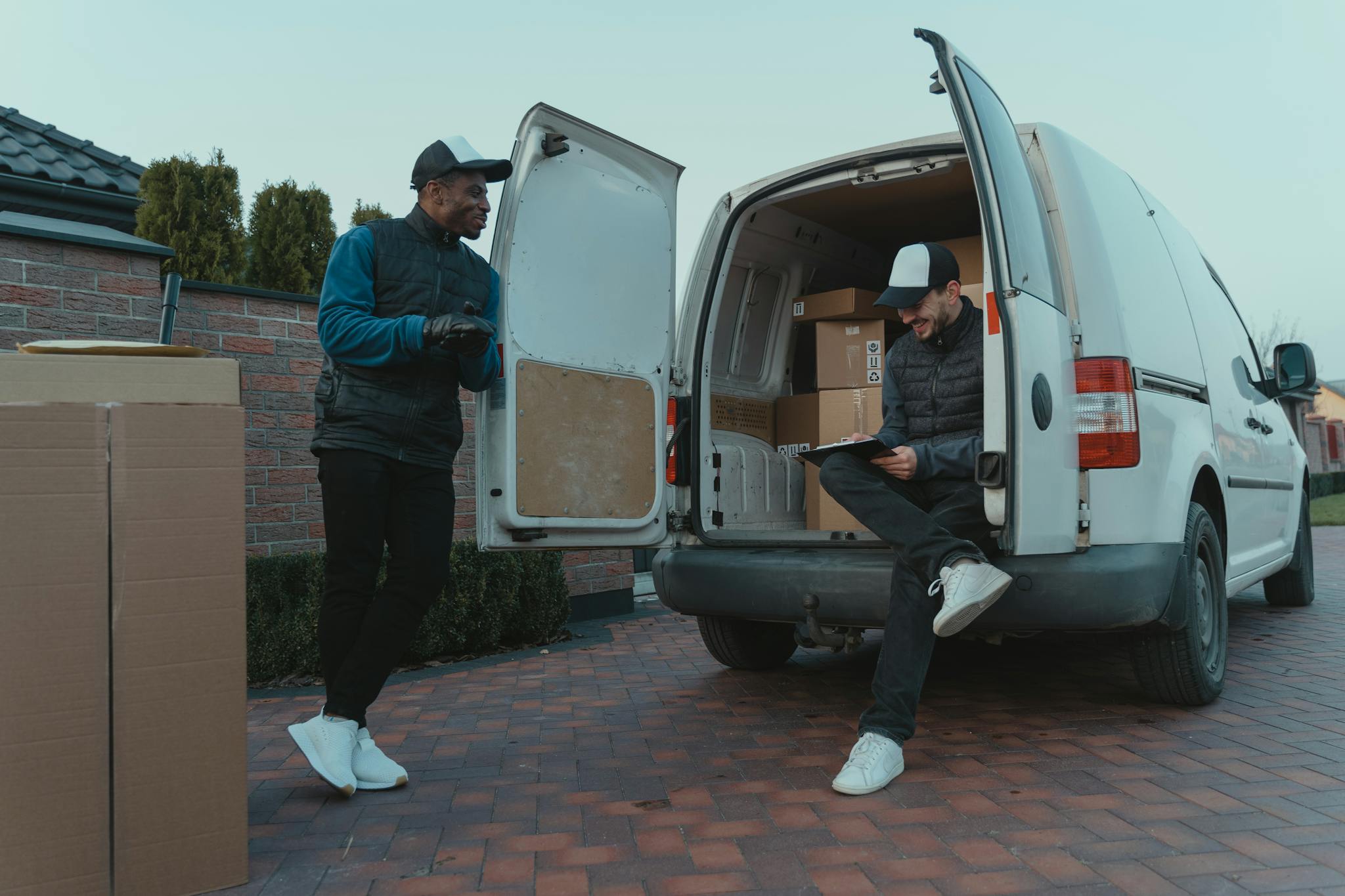 Two delivery workers loading packages into a van on a residential street.